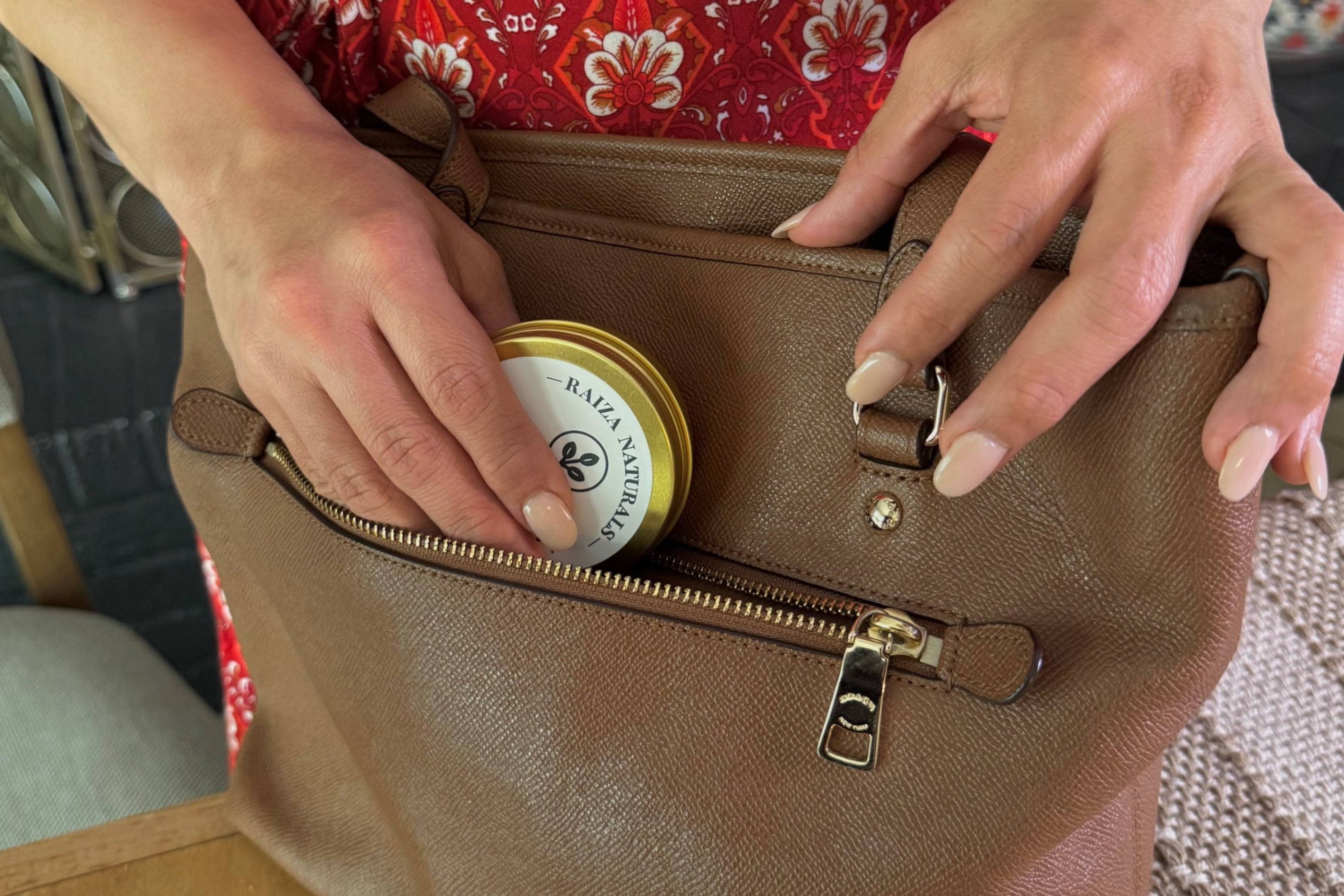 Person opening a brown leather handbag to reveal a container with a visible brand logo.